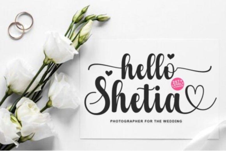 Puede incluir: Una tarjeta blanca con las palabras "hello Shetia" en escritura negra, con un s&iacute;mbolo de coraz&oacute;n. La tarjeta tambi&eacute;n dice "Fot&oacute;grafo para la boda". Rosas blancas y anillos de boda dorados tambi&eacute;n est&aacute;n en la imagen.