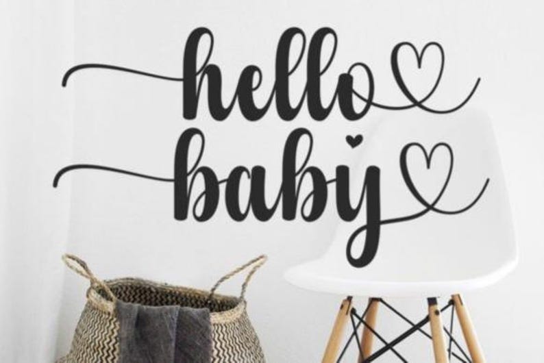 Puede incluir: Texto negro "hello baby" con corazones en una pared blanca. Una silla blanca con patas de madera y una cesta tejida con una manta gris en primer plano. Tema: decoraci&oacute;n de beb&eacute;s y guarder&iacute;as.