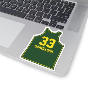 May include: A sticker in the shape of a green and yellow basketball jersey. The jersey has the number 33 and the name SAMUELSON in yellow block letters. The sticker is on a laptop.