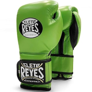 May include: A pair of green leather boxing gloves with black trim. The gloves have the text "Cleto Reyes" and "Hecho en Mexico" on them. The gloves are professional grade.