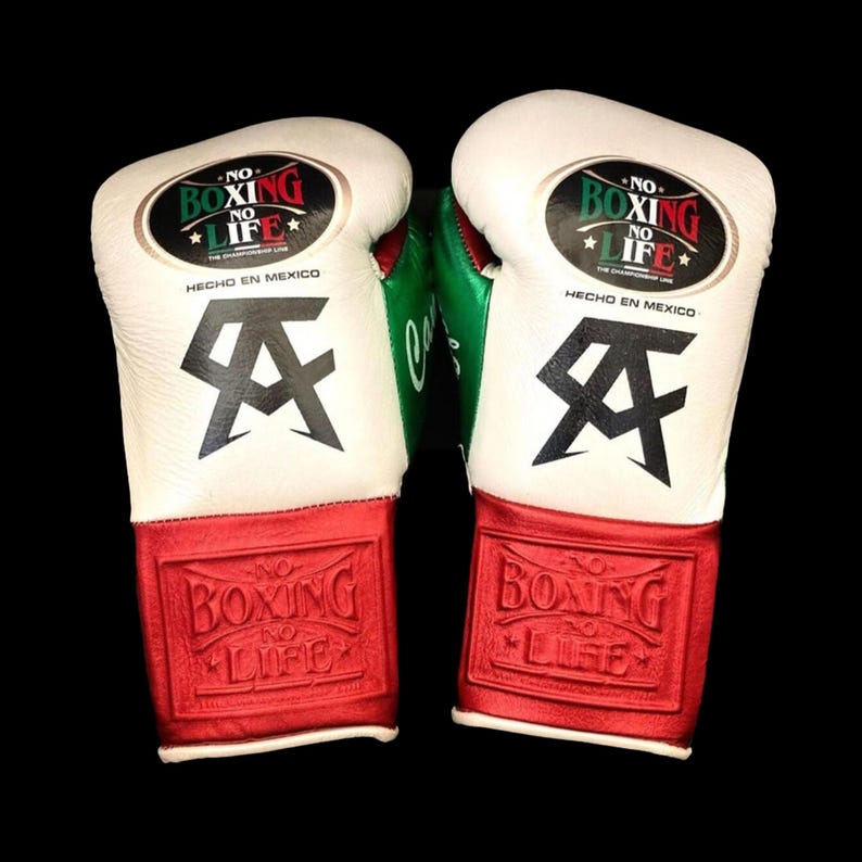 K&ouml;nnte beinhalten: Paar Boxhandschuhe mit wei&szlig;en, roten und gr&uuml;nen Akzenten. Die Handschuhe zeigen den Text "NO BOXING NO LIFE" und "HECHO EN MEXICO". Auf den Handschuhen ist auch ein schwarzes Logo mit den Buchstaben "AA" zu sehen.