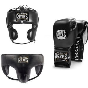 May include: Black boxing headgear, gloves, and groin protector set. The headgear has ear protection and a chin strap. The gloves are laced up. Each item has the "REYES" logo.