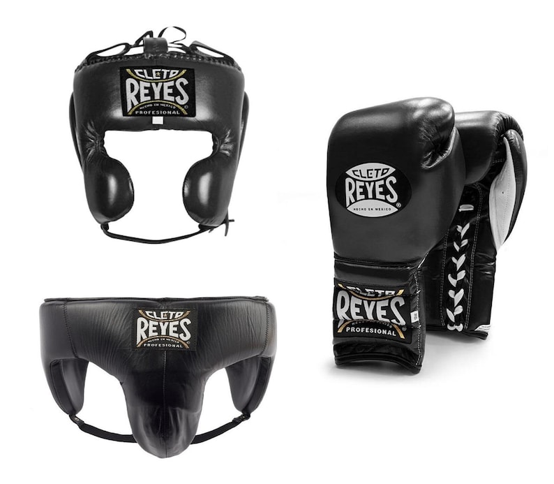 May include: Black boxing headgear, gloves, and groin protector set. The headgear has ear protection and a chin strap. The gloves are laced up. Each item has the "REYES" logo.