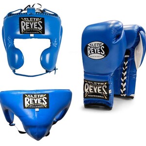 May include: A set of blue boxing equipment, including a headgear, a pair of gloves, and a groin protector. Each item features the "REYES" logo in black and gold. The gloves have white laces.