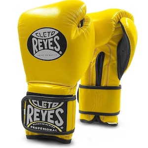 May include: A pair of yellow leather boxing gloves with black trim and the Cleto Reyes logo. The gloves have a velcro strap and are labeled "Hecho en Mexico" and "Professional".