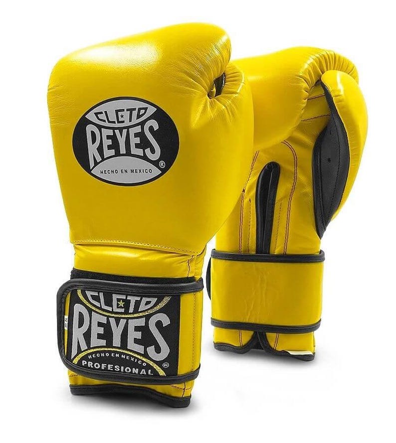 May include: A pair of yellow leather boxing gloves with black trim and the Cleto Reyes logo. The gloves have a velcro strap and are labeled "Hecho en Mexico" and "Professional".