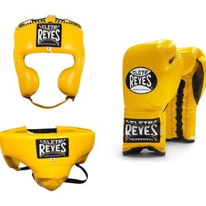 May include: Yellow boxing headgear, gloves, and groin protector set. The headgear and groin protector have the "REYES" logo. The gloves are yellow with black laces and the "REYES" logo. The set is designed for professional boxing.