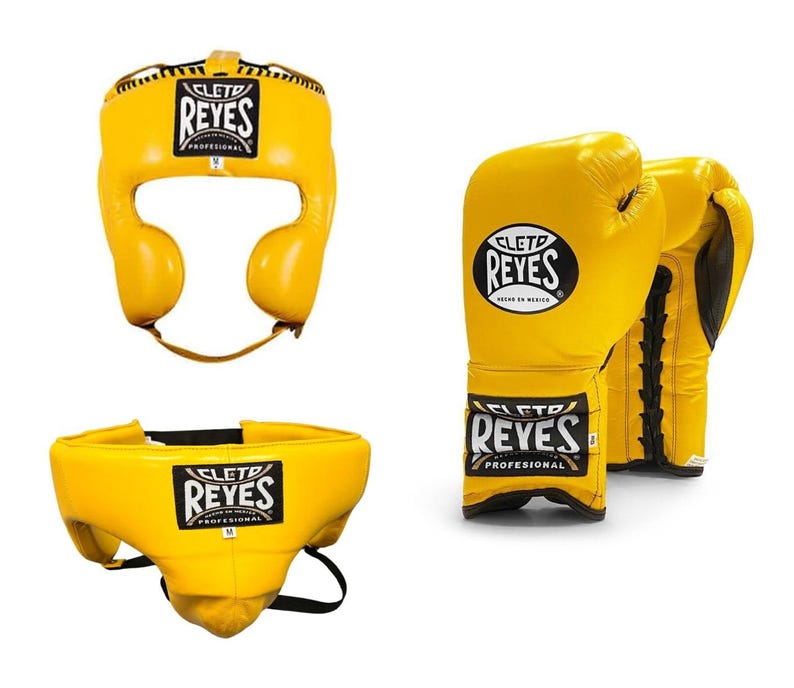 May include: Yellow boxing headgear, gloves, and groin protector set. The headgear and groin protector have the "REYES" logo. The gloves are yellow with black laces and the "REYES" logo. The set is designed for professional boxing.