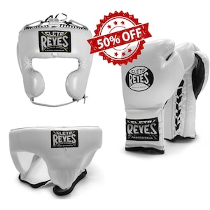 May include: White boxing headgear, gloves, and groin protector set. The headgear and groin protector have the "CLET0 REYES" logo. The gloves are white with black accents and lace-up closures. A red "50% OFF" sticker is in the background.
