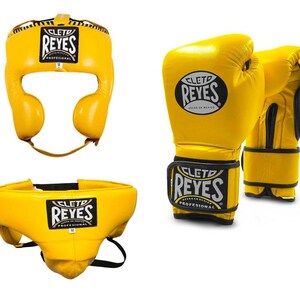 May include: Yellow boxing headgear, gloves, and groin protector set. The headgear has ear and face protection. The gloves are padded with a wrist strap. The groin protector has a black strap. All items have the "REYES" logo.