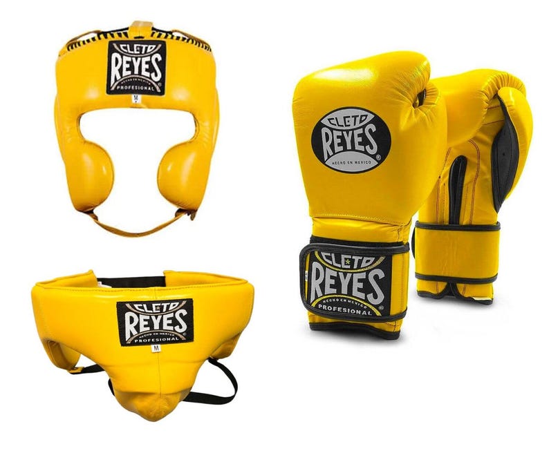 May include: Yellow boxing headgear, gloves, and groin protector set. The headgear has ear and face protection. The gloves are padded with a wrist strap. The groin protector has a black strap. All items have the "REYES" logo.