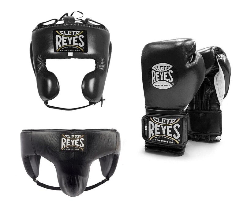 May include: Black boxing headgear, gloves, and groin protector set. The headgear has ear protection and a lace-up closure. The gloves and groin protector have the "REYES" logo. The gloves are black with white accents.