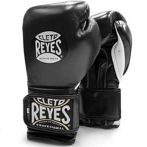 May include: Black leather boxing gloves with white accents. The gloves have the Cleto Reyes logo with the text "Cleto Reyes" and "Hecho en Mexico" on the front. The wrist strap has the text "Cleto Reyes" and "Profesional" on it.