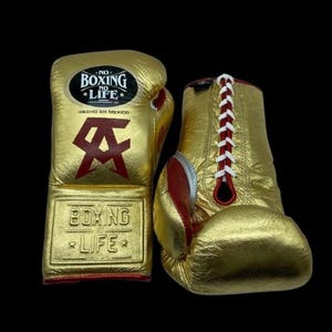 K&ouml;nnte beinhalten: Goldene Boxhandschuhe mit roten Akzenten und wei&szlig;en Schn&uuml;rsenkeln. Die Handschuhe zeigen den Text "NO BOXING NO LIFE" und "BOXING LIFE". Hergestellt in Mexiko.