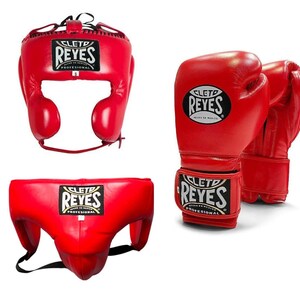 May include: Red boxing headgear, gloves, and groin protector set. The headgear has ear and cheek protection. The gloves are designed for boxing. The groin protector has a black strap. All items have the "REYES" logo.
