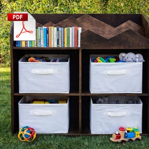 Puede incluir: Una estantería de madera marrón oscuro con una parte superior en forma de montaña, llena de libros coloridos, contenedores de almacenamiento blancos y juguetes. Los contenedores contienen juguetes y un elefante de peluche. Un tren de juguete colorido y una pelota están en el estante inferior.