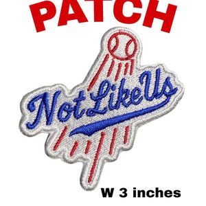 May include: Embroidered patch with the words "Not Like Us" in blue script, outlined in white, with a baseball graphic and the word "PATCH" in red. The patch is 3 inches wide and 2.75 inches high.