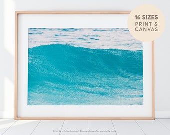 May include: A photograph of a large, turquoise blue wave crashing in the ocean. The wave is breaking and creating a foamy crest. The water is clear and blue, and the sky is a light blue.