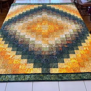 May include: A handmade quilt with a geometric design. The quilt features a central diamond pattern in shades of yellow, orange, and green, with a dark green border. The quilt is made of fabric squares and is likely used as a bed covering.