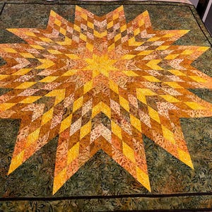 May include: A large, handmade quilt featuring a vibrant starburst design. The star is composed of diamond-shaped patches in shades of yellow, orange, and brown, radiating from a central point. The background is a dark green with a leaf pattern, and the quilt has a black border.