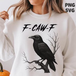 May include: White sweatshirt with a black raven illustration perched on a branch. The text "F-CAW-F" is printed above the raven. The design has a gothic or Halloween theme, with a dark and mysterious aesthetic.