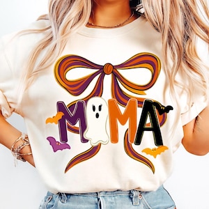Könnte beinhalten: Cremefarbenes Sweatshirt mit einem Halloween-Motiv. Das Wort "MAMA" ist in Lila, Orange und Schwarz dargestellt, mit einem Geist anstelle des zweiten "M". Eine große Schleife und Fledermäuse vervollständigen das Design.