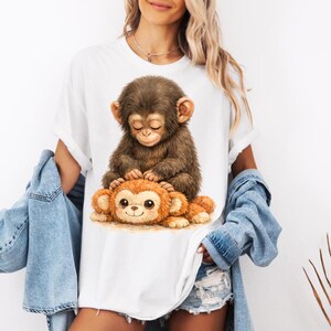Peut inclure: T-shirt blanc avec une illustration d&eacute;taill&eacute;e de deux singes de dessin anim&eacute;. L'un est brun et assis, l'autre orange et allong&eacute;. Le motif est centr&eacute;, cr&eacute;ant une esth&eacute;tique ludique et fantaisiste, id&eacute;ale pour un usage d&eacute;contract&eacute;.
