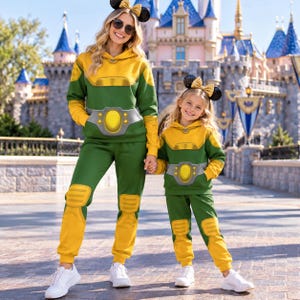 May include: Two matching sets of green and yellow hooded sweatshirts and sweatpants featuring a printed belt and knee pad design. Each set is paired with black mouse ear headbands adorned with gold sequin bows, worn with white trainers.