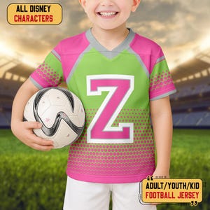 May include: A child's green and pink football jersey with a large pink letter "Z". The jersey has grey accents and the text "ALL DISNEY CHARACTERS" and "ADULT/YOUTH/KID FOOTBALL JERSEY". The child is holding a soccer ball.