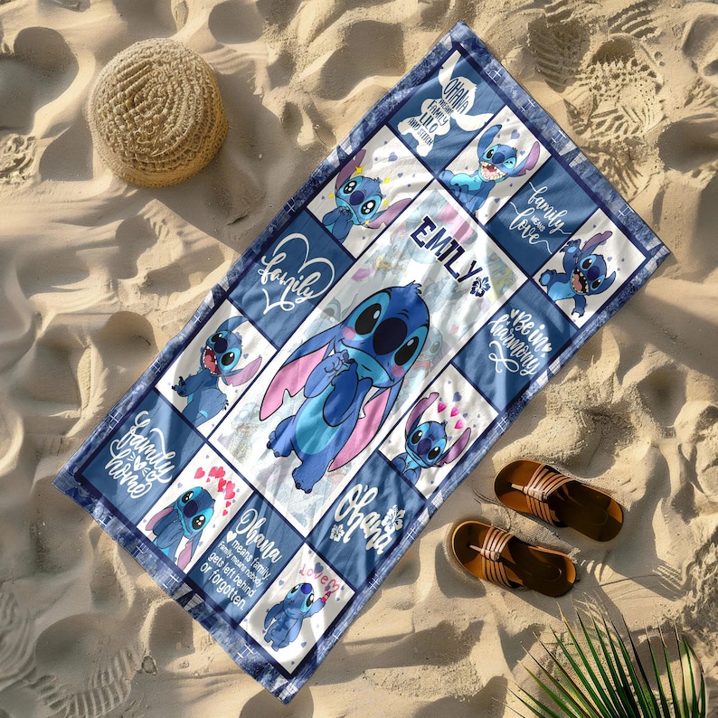 May include: A blue and white beach towel featuring the character Stitch from Lilo & Stitch. The towel has a grid pattern with Stitch illustrations, the name "EMILY", and the words "Family", "Ohana", and "Love". The towel is rectangular and is on a sandy surface.