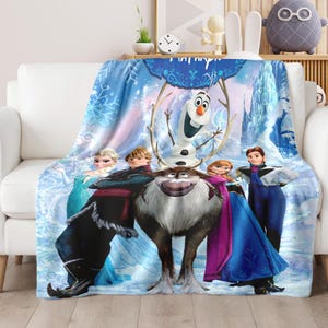 Puede incluir: Una manta azul con personajes de la pel&iacute;cula "Frozen". El dise&ntilde;o incluye a Elsa, Anna, Kristoff, Olaf y Sven, sobre un fondo nevado y helado con un castillo.