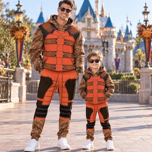 May include: Matching orange and brown hooded sweatshirts and sweatpants featuring a printed armor design with textured fur-like patterns on the sleeves and legs. Both sets include black accents and are worn with white sneakers and dark sunglasses.