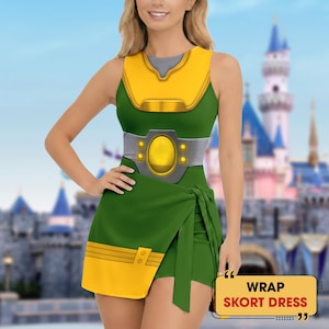 May include: A sleeveless skort dress featuring a green and yellow color scheme with a printed graphic of a metallic belt and chest plate. The garment includes a wrap-style skirt with a yellow hem and a yellow bodice section. Text reads WRAP SKORT DRESS.