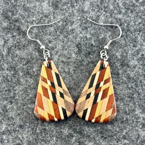 May include: A pair of wooden earrings with a geometric design. The earrings are made of various wood tones, including light brown, dark brown, black, and orange. The earrings hang from silver-coloured fish hook ear wires.