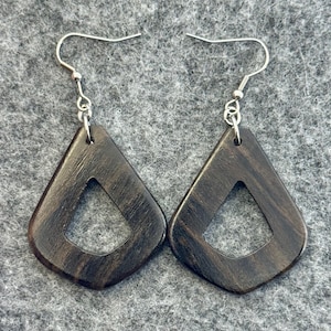 May include: A pair of dark brown wooden earrings. Each earring has a geometric, diamond-like shape with a cut-out triangle in the centre. The earrings hang from silver-coloured fish hook ear wires.