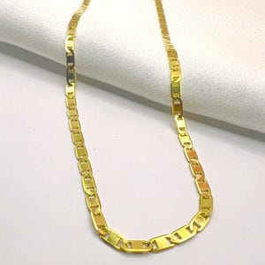 May include: A gold-colored chain necklace with a flat, rectangular link design. The necklace is displayed on a white, textured surface. The chain is a bright, shiny gold color.