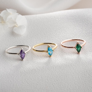 Könnte beinhalten: Drei zarte Ringe mit marquiseförmigen Edelsteinen in Lila, Blau und Grün. Die Ringe haben silberne, goldene und roségoldene Bänder. Die Edelsteine sind der Blickfang der Ringe.