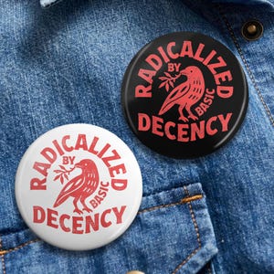 Peut inclure: Deux badges ronds avec le texte "RADICALIZED BY BASIC DECENCY" en rouge. Un badge est blanc avec du texte rouge et un graphisme d'oiseau rouge. L'autre badge est noir avec du texte rouge et un graphisme d'oiseau rouge. Les badges sont sur un fond en denim bleu.