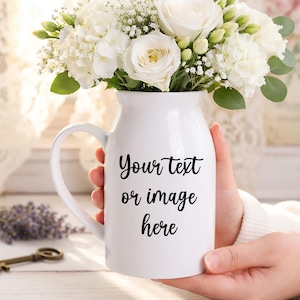 May include: A white ceramic mug with a black handle and the text "But First, Coffee" in a black, handwritten-style font. The mug is on a white surface.