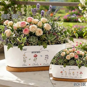 May include: A white ceramic planter filled with roses, succulents, and lavender. The planter has the words "FIRST mom" and names "Olivia, Charles, Madeline" on the front. The back says "NOW grandma" with names.