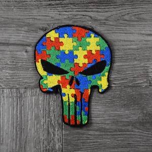 Könnte beinhalten: Ein gestickter Schädel in Schwarz und Weiß mit einem Puzzle-Muster in Rot, Gelb, Blau und Grün.