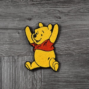 May include: Yellow embroidered Winnie the Pooh cartoon character patch with red shirt and black outline.