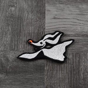 May include: White embroidered patch of a ghost-like character with an orange nose, flying with its arms outstretched. The character is from the movie "The Nightmare Before Christmas".