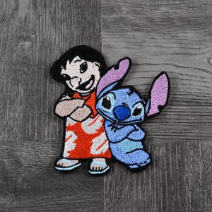 Op de afbeelding: Geborduurde strijkpatch met Lilo en Stitch uit de Disney-film Lilo & Stitch. Lilo draagt een rood-witte jurk en Stitch is blauw met een roze oor.