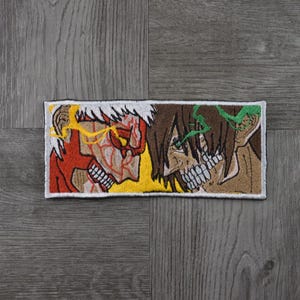 May include: Embroidered patch featuring two anime characters facing each other. The character on the left has red and yellow hair and a red and yellow body. The character on the right has brown hair and a green and brown body.