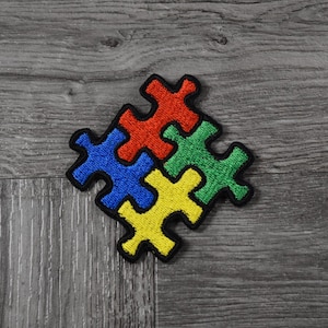 May include: Four puzzle pieces, each a different colour: blue, red, green, and yellow, are arranged in a square shape on a grey wooden surface.