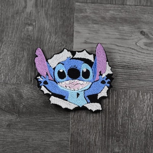 Op de afbeelding: Blauwe en paarse geborduurde strijkpatch van Stitch uit Lilo & Stitch, die uit een gescheurd gat kijkt.