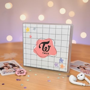 Puede incluir: Una caja blanca con un patrón de cuadrícula y un logotipo rosa que dice "TWICE" en negro. La caja está decorada con pegatinas de estrellas y flores. También se ve una tarjeta fotográfica y un pin con el mismo logotipo.