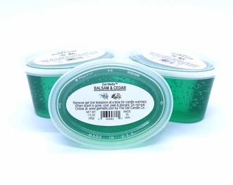 以下が含まれることがあります： Gel Melts Balsam & Cedarとラベルが貼られた、緑色のジェルワックスが入った3つの楕円形容器。透明なプラスチック製の蓋には、使用説明、バーコード、正味重量42グラムの記載があります。アメリカ製。