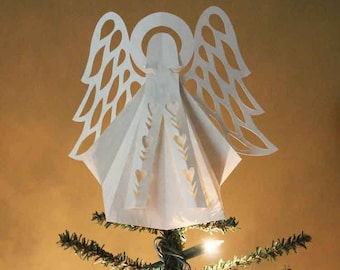 May include: A white paper angel tree topper with intricate cutouts in the wings and a halo. The angel is standing on a green artificial Christmas tree.